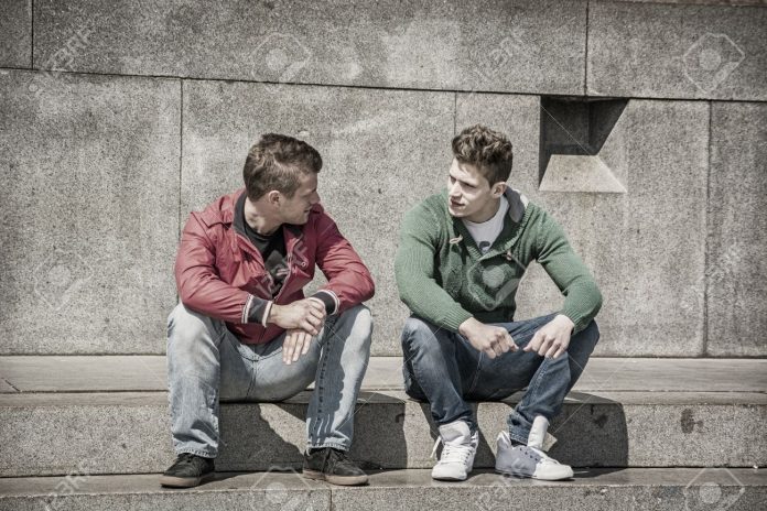 Two young men talking while sitting on curb